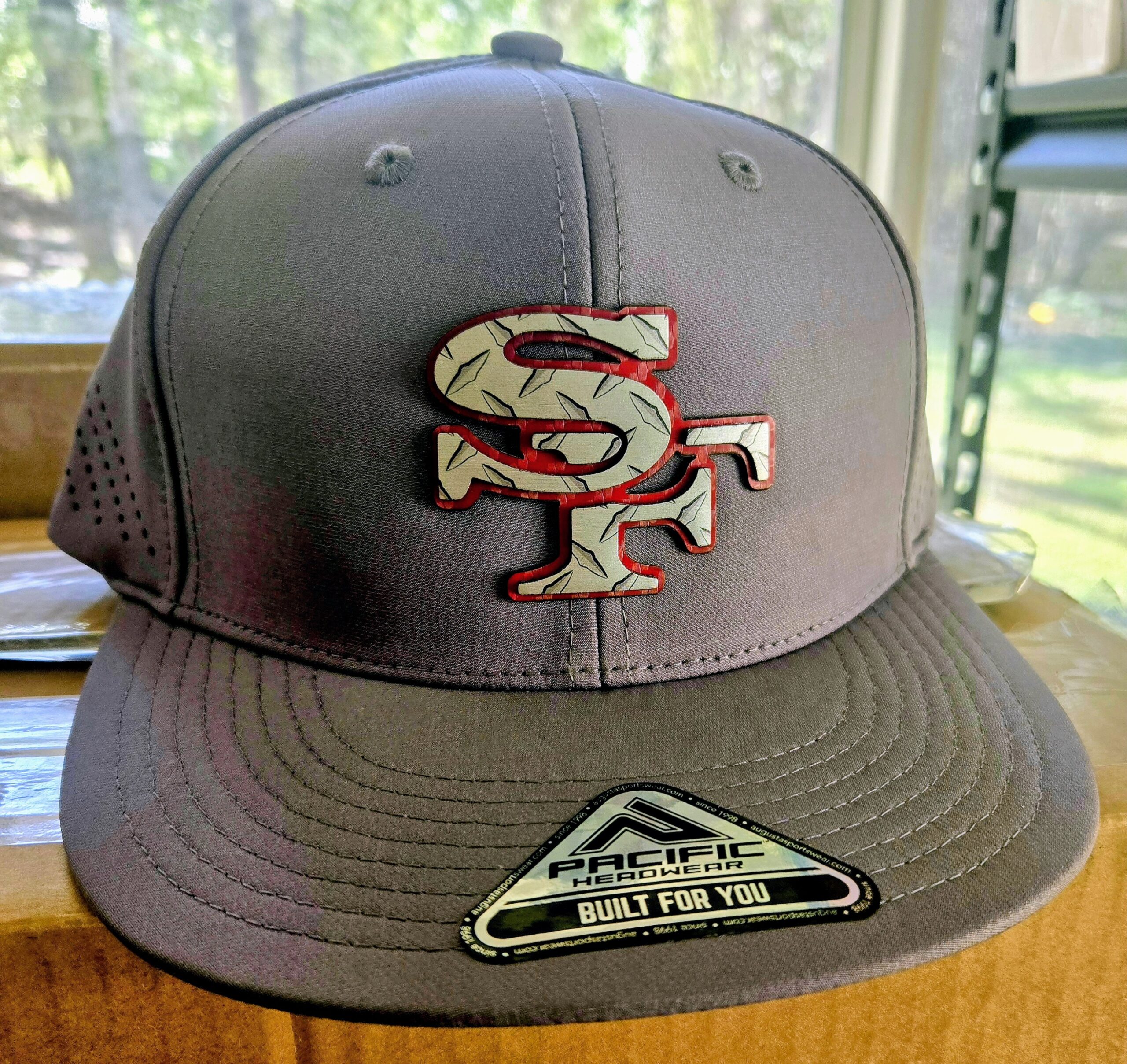 Gray SF baseball cap with red and white logo on a window sill.