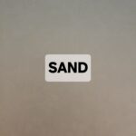 A beige surface with the word 'SAND' in bold black letters on a white label.